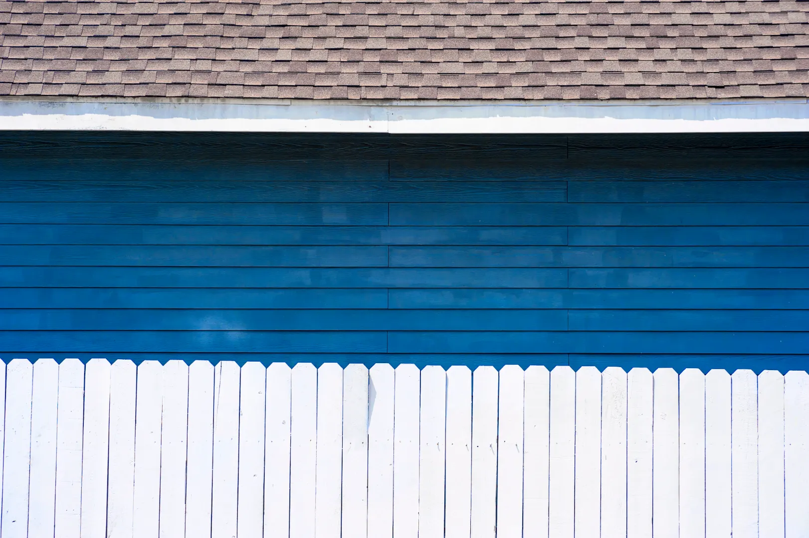 Blue painted wood siding on a house with white trim and a picket fence